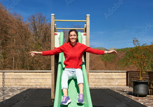young woman in a red sweater jumps down a green slide