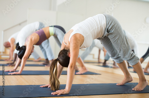 Young adult sporty woman practicing yoga with group at class