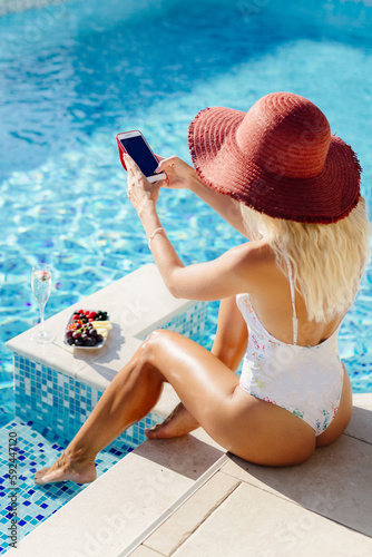 woman relax in swimming pool outdoors. Beautiful female model in swimsuit drink champagne and eat fruits. Summer vacation time in luxury resort.