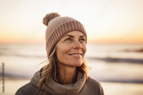 Portrait of smiling woman in hat and scarf standing on beach at sunset © Robert MEYNER