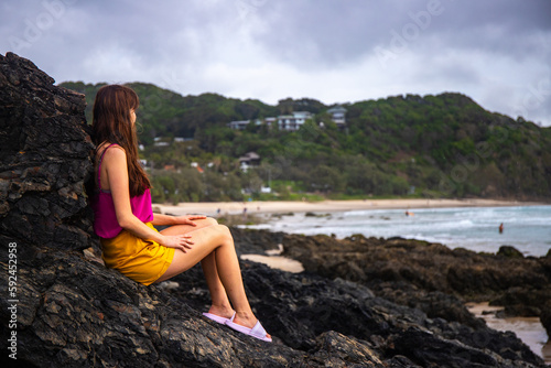 Beautiful girl stand on large rocks and admires powerful  waves in popular Byron Bay, NSW, Australia