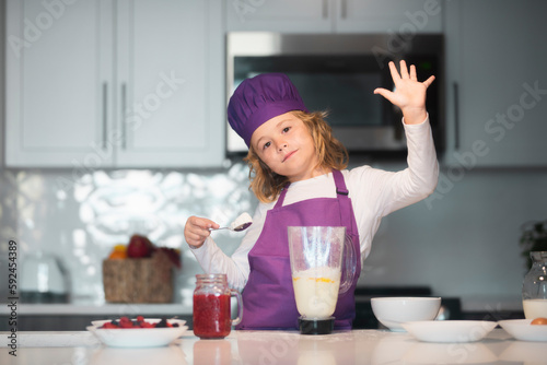 Kid cooking. Funny little kid chef cook wearing uniform cook cap and apron cooked food in the kitchen.