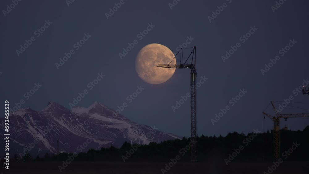 Large full moon rising behind construction crane, Reykjavik Iceland time lapse