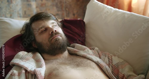 Pensive shabby, unkempt man with careless beard and unwashed long hair lying on the coach thoughtful. Lazy slacker careless lifestyle