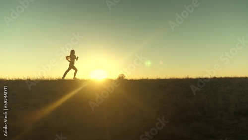 running after sun. training jogging. A healthy beautiful girl is engaged in fitness  jogging in country in sun. Jogger girl breathes fresh air on field. Free young woman runs in summer park at sunset.