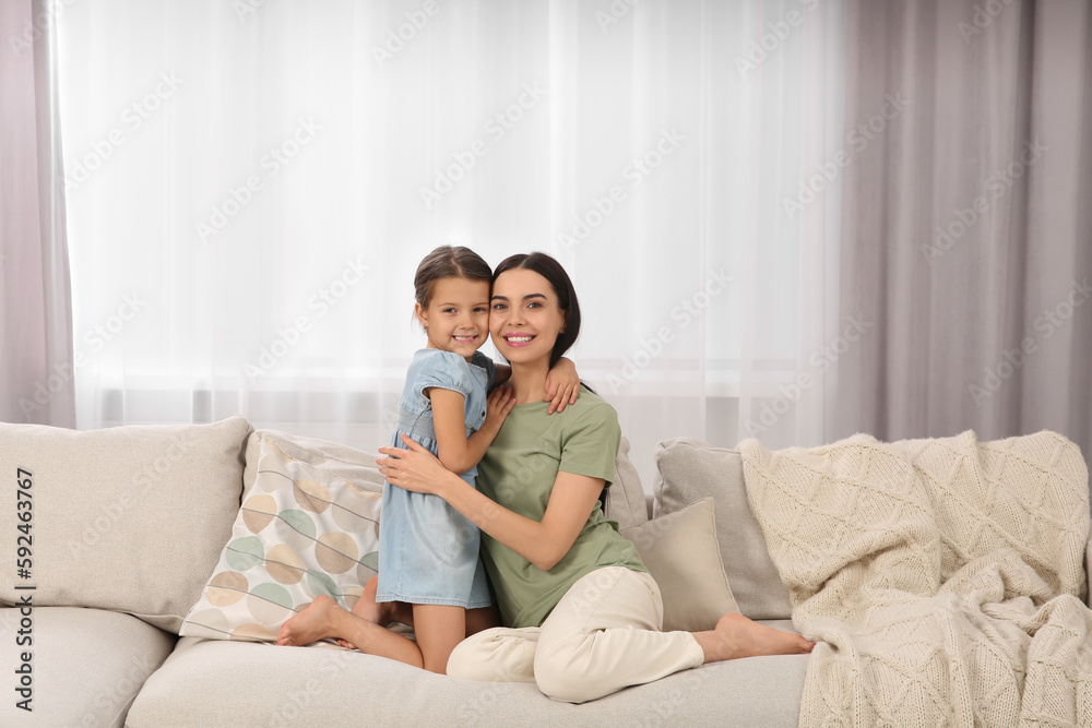 Happy woman and her cute daughter spending time together on sofa at home. Mother's day celebration