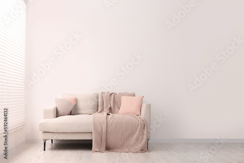 Cozy sofa with pillows and blanket in living room, space for text. Interior design