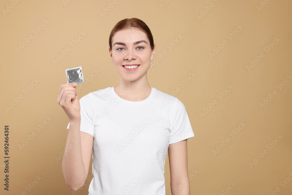 Woman holding condom on beige background, space for text. Safe sex Woman holding condom on beige background, space for text. Safe sex