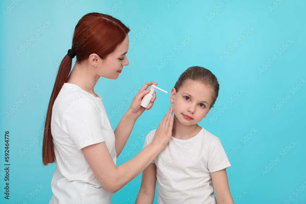 Mother spraying medication into daughter's ear on light blue background Mother spraying medication into daughter's ear on light blue background