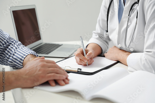 Doctor consulting patient at white table indoors, closeup