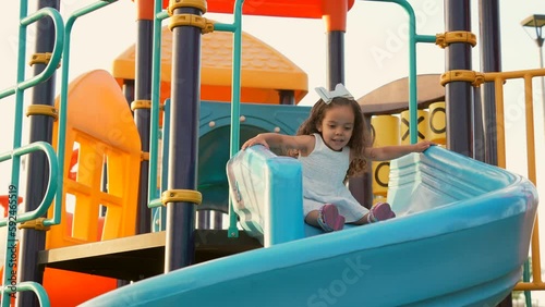 Niña hermosa latina disfrutando y jugando en los juegos de un parque en el resbaladero deslizándose en el tobogán divertida en una bonita área de juegos en un hermoso día soleado al aire libre photo