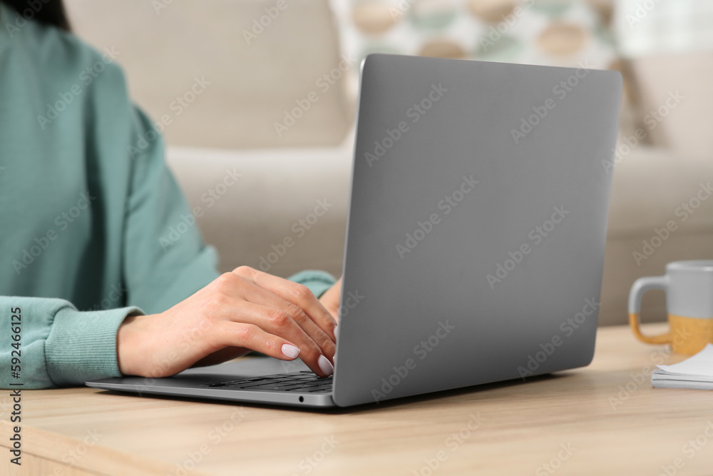 Woman working with laptop at wooden desk indoors, closeup Woman working with laptop at wooden desk indoors, closeup