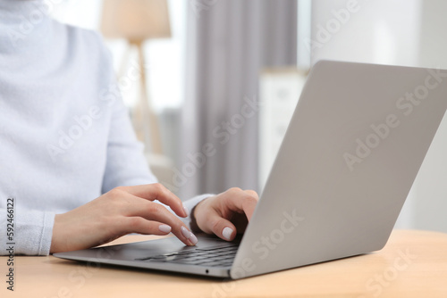 Woman working with laptop at wooden desk indoors, closeup