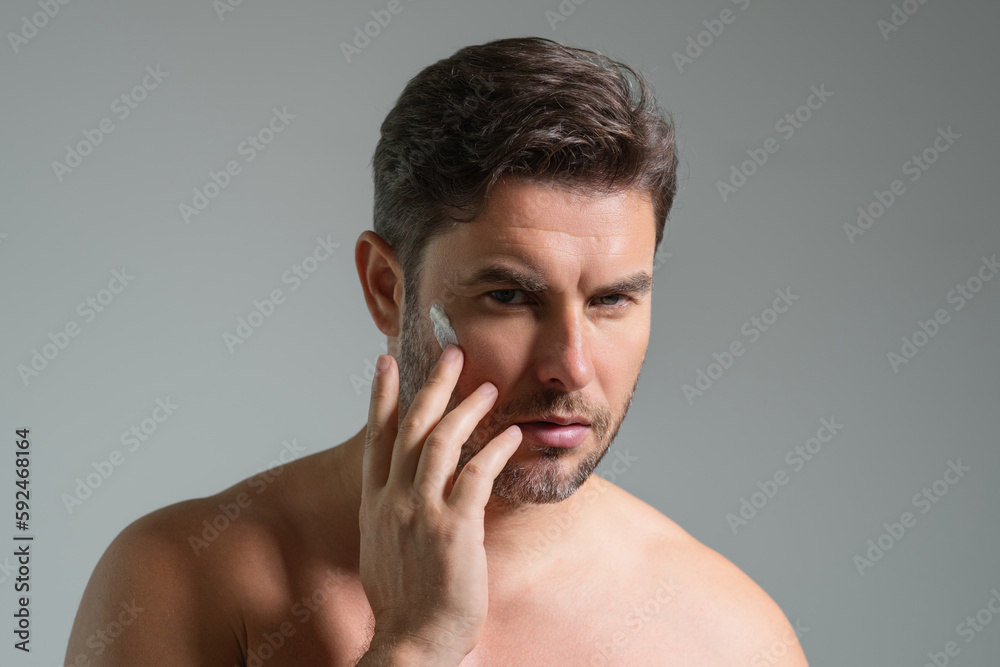 Obraz premium Close up portrait of man 40s applying cream on face. Handsome serious man enjoy fresh perfect skin, applying cream. Portrait of beauty man with cosmetic cream on skin. Man with cream on face.