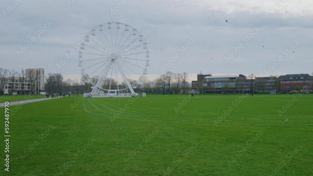 Pan across white Ferris wheel behind green grass track in Cambridge England Pan across white Ferris wheel behind green grass track in Cambridge England