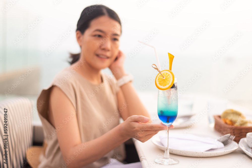 Happy asian woman drinking flavored cocktails on a rooftop with beautiful sunset Happy asian woman drinking flavored cocktails on a rooftop with beautiful sunset