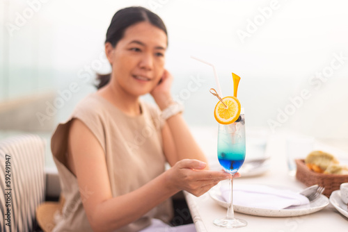 Happy asian woman drinking flavored cocktails on a rooftop with beautiful sunset