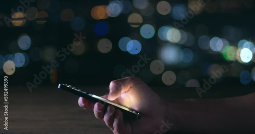 Male hand scrolling browsing on a smartphone at night time. Close-up of person using smartphone, browsing social network. Cinematic shot of male hand scroll through news feed on app on his smartphone. photo