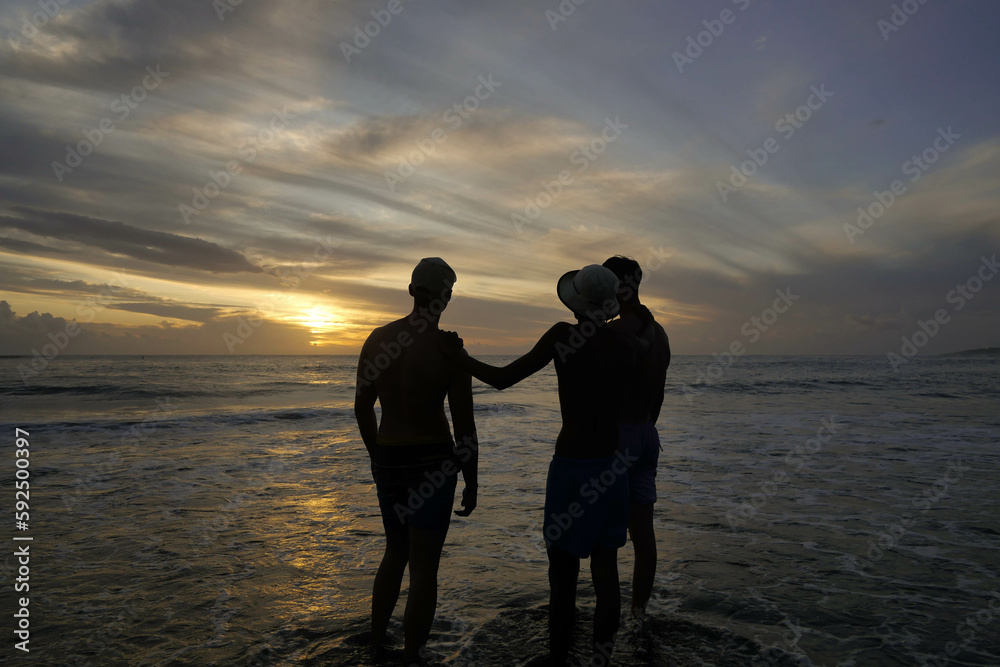 Trois amis devant un coucher de soleil sur une plage de l'île de la réunion.