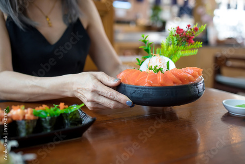 Woman holding salmon sashimi in black bowl on wood table background, Japanese style