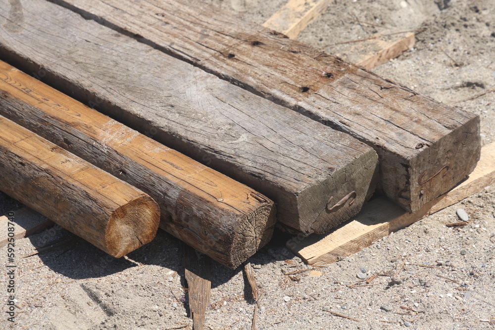 Old wooden beams and sleepers lie on the sand at a construction site, close-up. Old wooden beams and sleepers lie on the sand at a construction site, close-up.