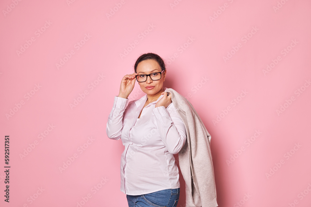 Portrait of serious pregnant business woman in casual shirt, looking at camera through stylish black framed eyeglasses, isolated over pink background. Business. People. Pregnancy. Maternity leave