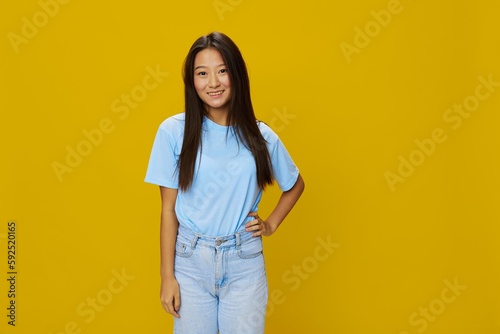 Asian woman smile with teeth hand gestures, signs and symbols on yellow background in blue t-shirt and jeans