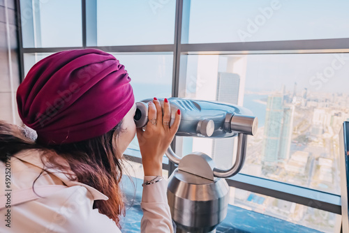 Billede på lærred Girl tourist at the observation viewpoint using binoculars and looking to Abu Dh