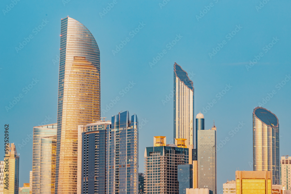 Naklejka premium Marvel at the breathtaking beauty of Abu Dhabi's towering buildings at sunset, iconic skyline that's recognized around the world.