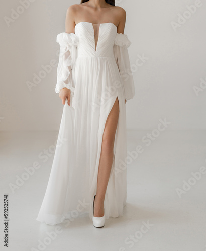 Gorgeous classic long wedding dress with cleavage and long sleeve decorated with floral lace. Bride in the shoulderless white wedding dress with deep neckline and long fancy wide see-through sleeves