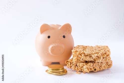 Instant noodles, a dried and precooked noodle block and piggy bank with coins isolated on white background. Saving money or financial hardship concept. Saving money in your daily life.
