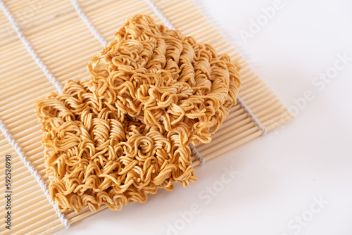 Instant noodles, a dried and precooked noodle block on bamboo mat isolated on white background.