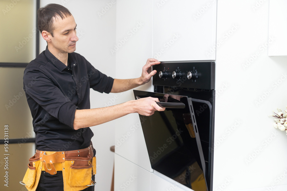 Don't delay with repair. Close-up of repairman examining oven with screwdriver in kitchen with tool case
