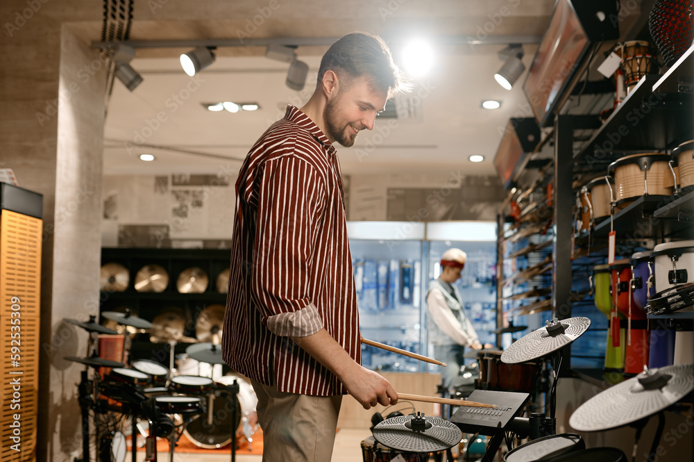 Young man buyer choosing drums at modern music shop