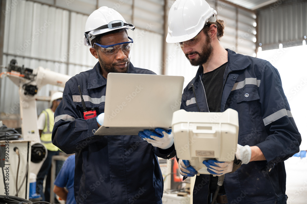 Caucasian and African American technician engineer man use remote control and computer notebook with checking machine arm robot at factory Caucasian and African American technician engineer man use remote control and computer notebook with checking machine arm robot at factory