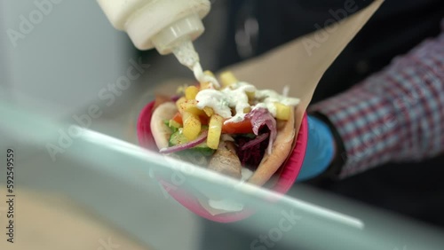 Cook pouring white tzatziki sauce on a gyros sandwich in a Greek restaurant kitchen photo