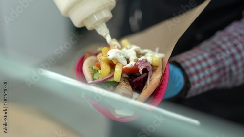 Cook pouring white tzatziki sauce on a gyros sandwich in a Greek restaurant kitchen