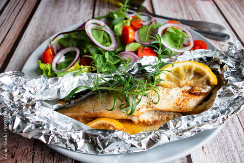 Mackerel baked in foil with vegetables on a plate. on a wooden background
