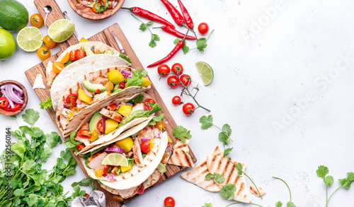 Tacos with grilled chicken fillet, salsa sauce, mango, cilantro and red onion in corn tortilla on cutting board. White table background, top view