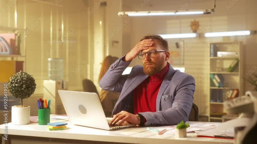 A middle aged man is typing on a laptop keyboard and is suffering from fever, sore throat and cough. A sick businessman works in the office at the table. A middle aged man is typing on a laptop keyboard and is suffering from fever, sore throat and cough. A sick businessman works in the office at the table.
