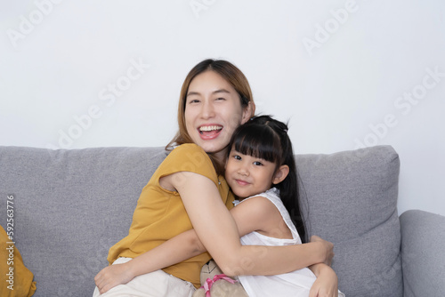 Asian Mother hug her daughter on couch in living room.