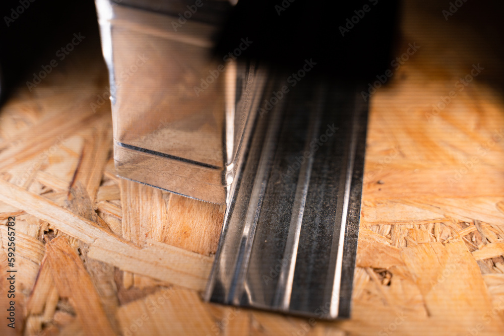 Cut with metal scissors and the curved edge of a thin metal U profile of stainless steel close-up on an oriented strand board at a construction site
