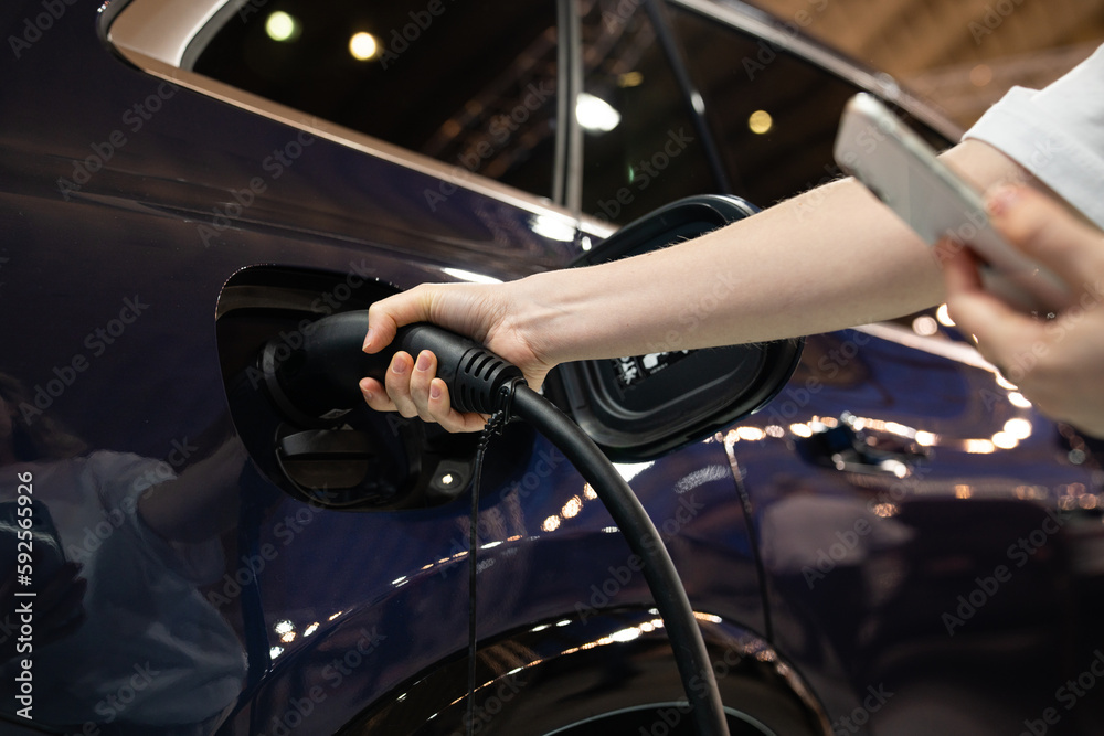 Naklejka premium Woman holding plug of electric car charging station 