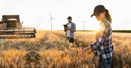 Couple of farmer with digital tablet on a background of harvester. Wind turbines on a horizon. Smart farming concept.