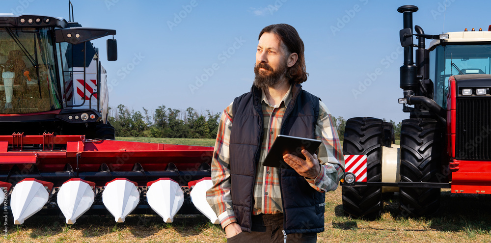 Farmer with digital tablet on a background of combine harvester and tractor. Smart farming concept.	
