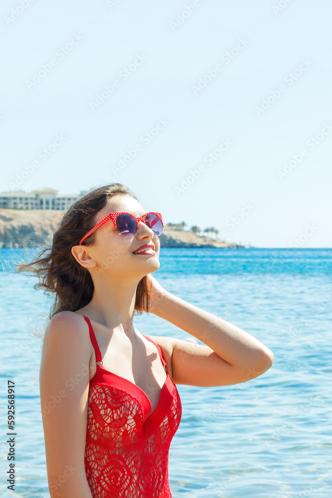 Beautiful happy brunette girl posing on the beach in a red bathing suit