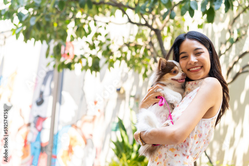 Asian woman playing with chihuahua dog at pets friendly dog park. Domestic dog with owner enjoy urban outdoor lifestyle in the city on summer vacation. Pet Humanization and urban pet parents concept.
