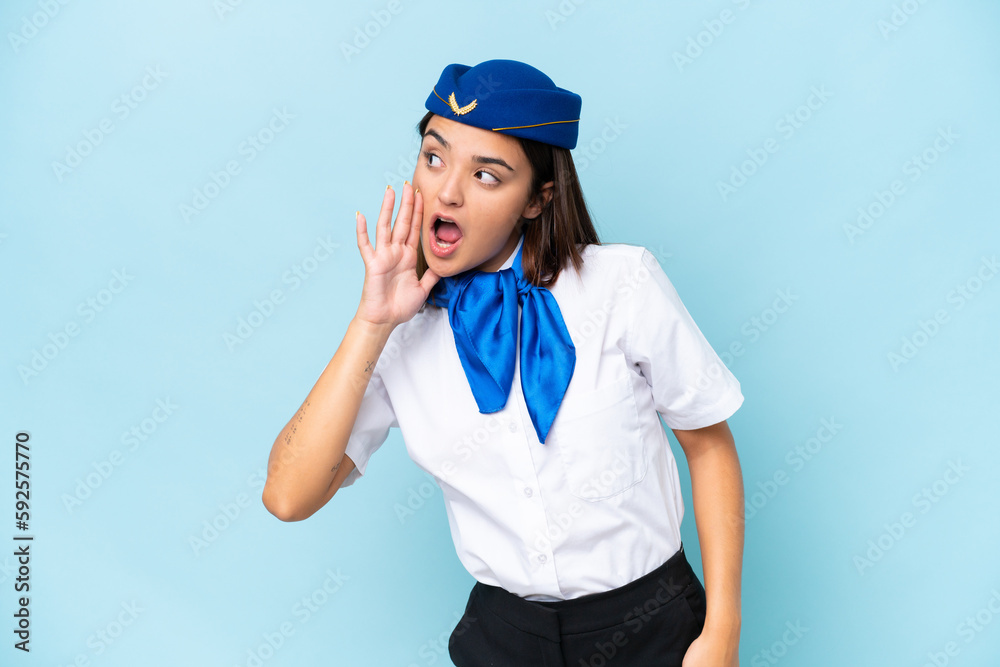Airplane stewardess caucasian woman isolated on blue background shouting with mouth wide open to the lateral Airplane stewardess caucasian woman isolated on blue background shouting with mouth wide open to the lateral