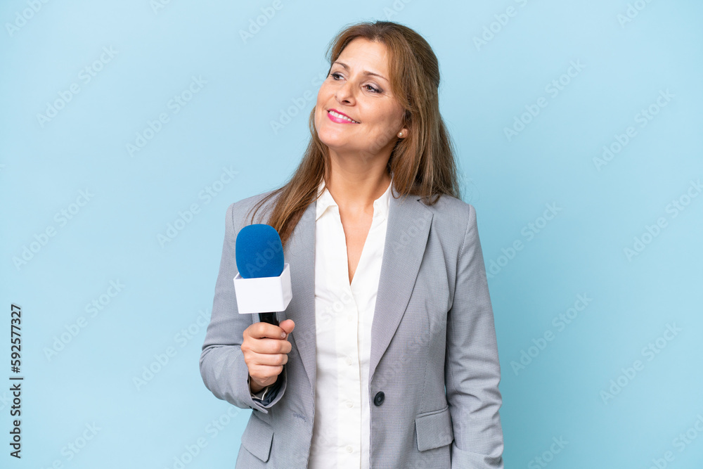 Middle-aged TV presenter woman over isolated blue background looking to the side and smiling Middle-aged TV presenter woman over isolated blue background looking to the side and smiling