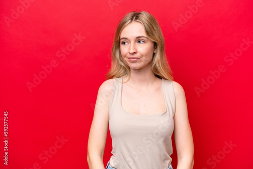 Young English woman isolated on red background having doubts while looking side